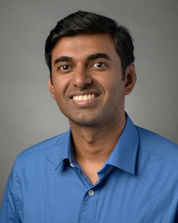 A man with brown hair and a blue shirt smiles at the camera.