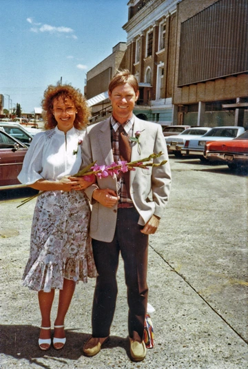 A man in a gray suit jacket poses for a photo with a women holding a bouquet.