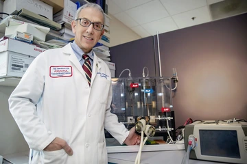 A man with gray hair wears a white lab coat.