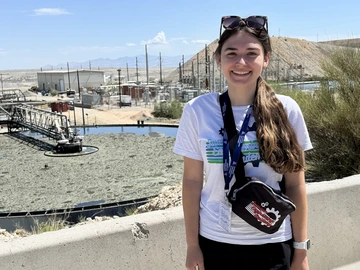 A woman with long brown hair stands in front of a copper mine.