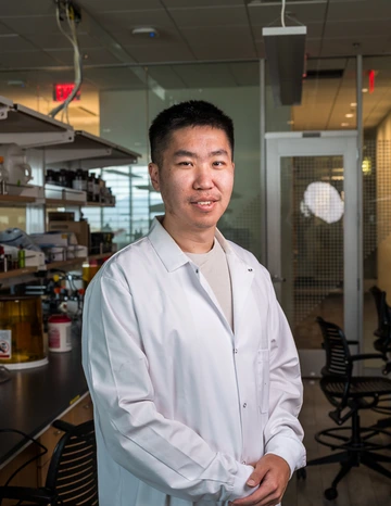 A student with dark hair wears a white lab coat.