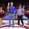 four people stand and wave from a basketball court.