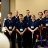 Six men and one woman pose for a photo next to a golfing robot.