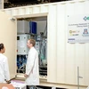 Two men in lab coats stand in front of a large metal shipping container.