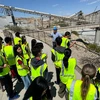 A group of students in yellow vests look over a railing at an open mine pit.