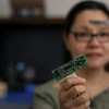 A woman with dark brown hair holds up a computer chip.