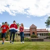 Three students in red shirts walk on a green lawn.