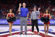 four people stand and wave from a basketball court.