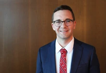 A man with brown hair poses for a photo in a blue blazer.