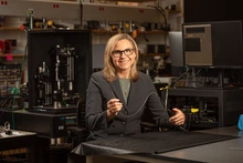 A woman with blond hair holds up a really tiny microscope.