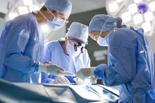 Three people in blue gowns perform surgery.