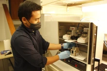 Suchol Savagatrup, wearing a face masks and blue latex gloves, reaches into a cabinet in his lab.