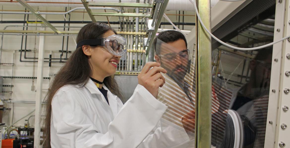 Two students wearing lab coats and goggles in a lab.