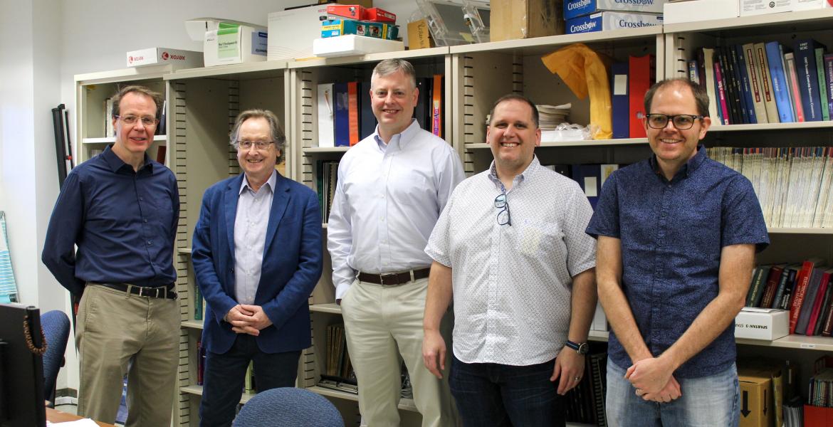 Five men pose for a photo in front of a bookshelf