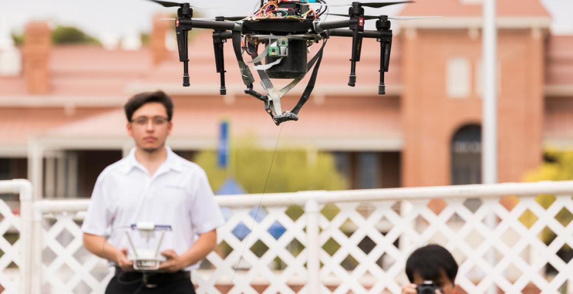 A student in a white polo shirt flies a tethered drone outside Old Main at Engineering Design Day