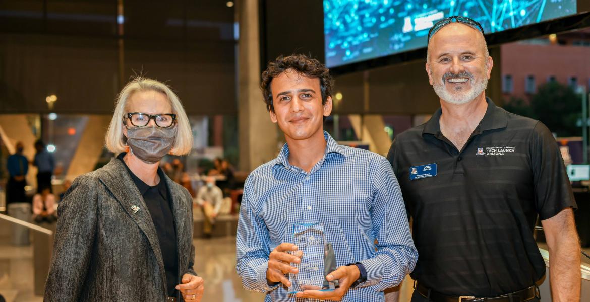 A woman and two men smile for a photo. Sahand Sabet, center, holds a glass award.