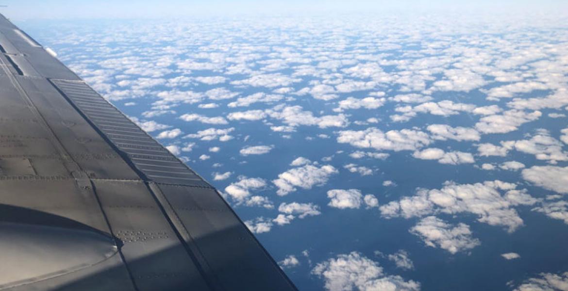 photo taken from a plane showing cumulus clouds from above. The wing of the plane is visible in the left of the frame