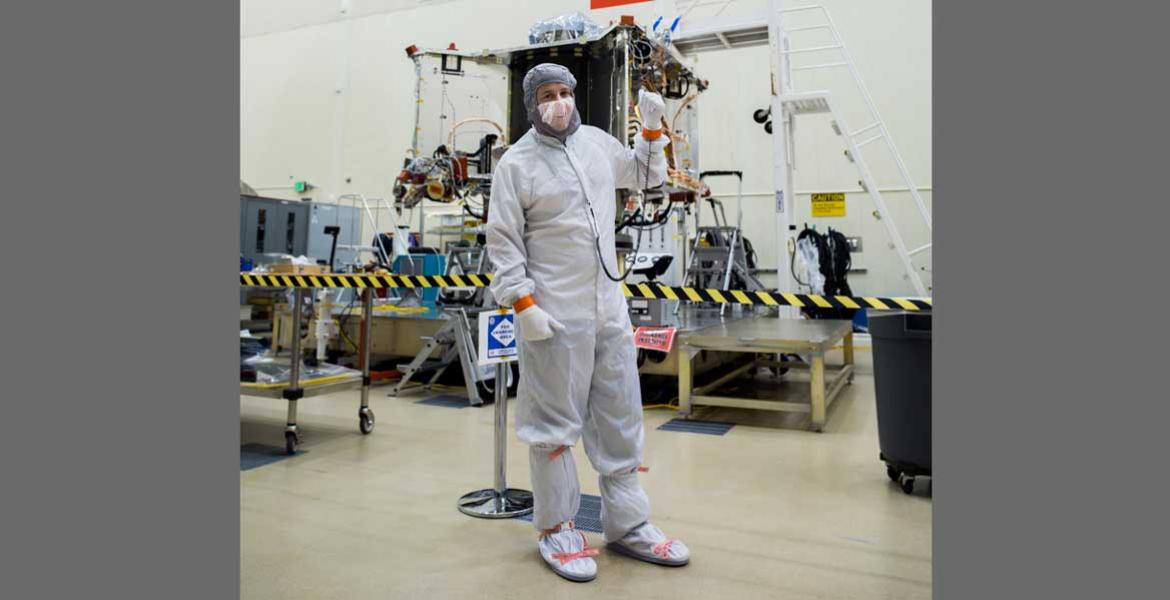 Bradley Williams in a white safety suit in front of a spacecraft.