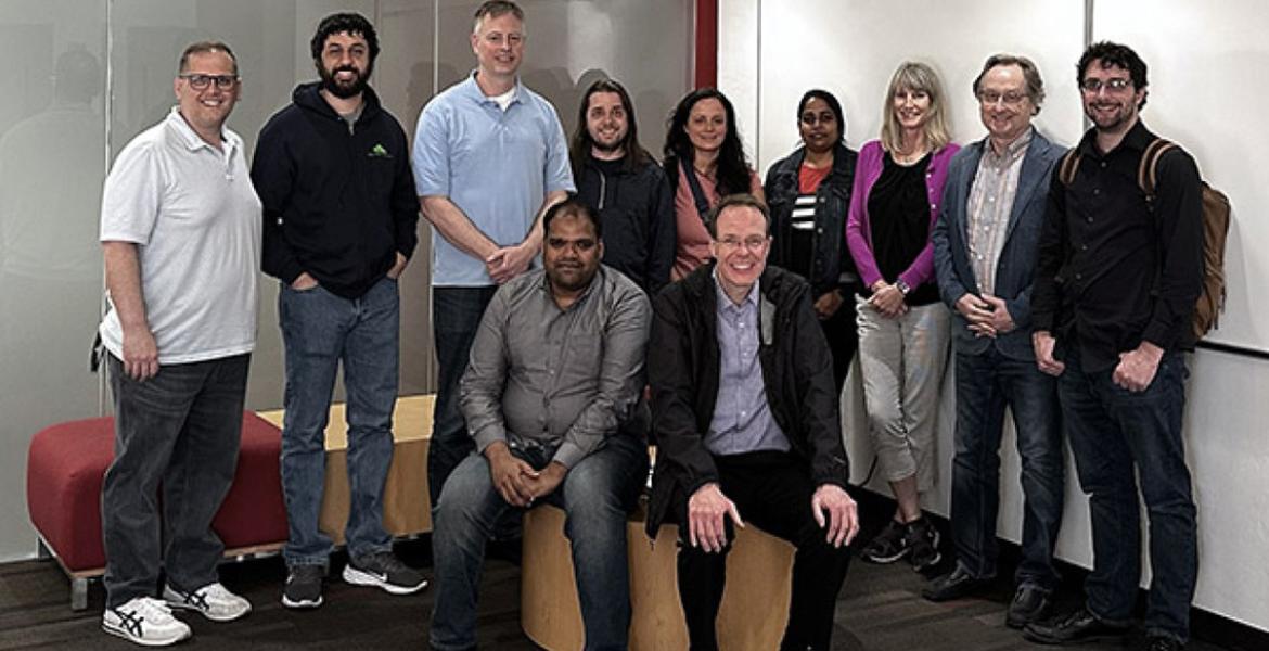 Team members pose in a room with a glass wall and whiteboard