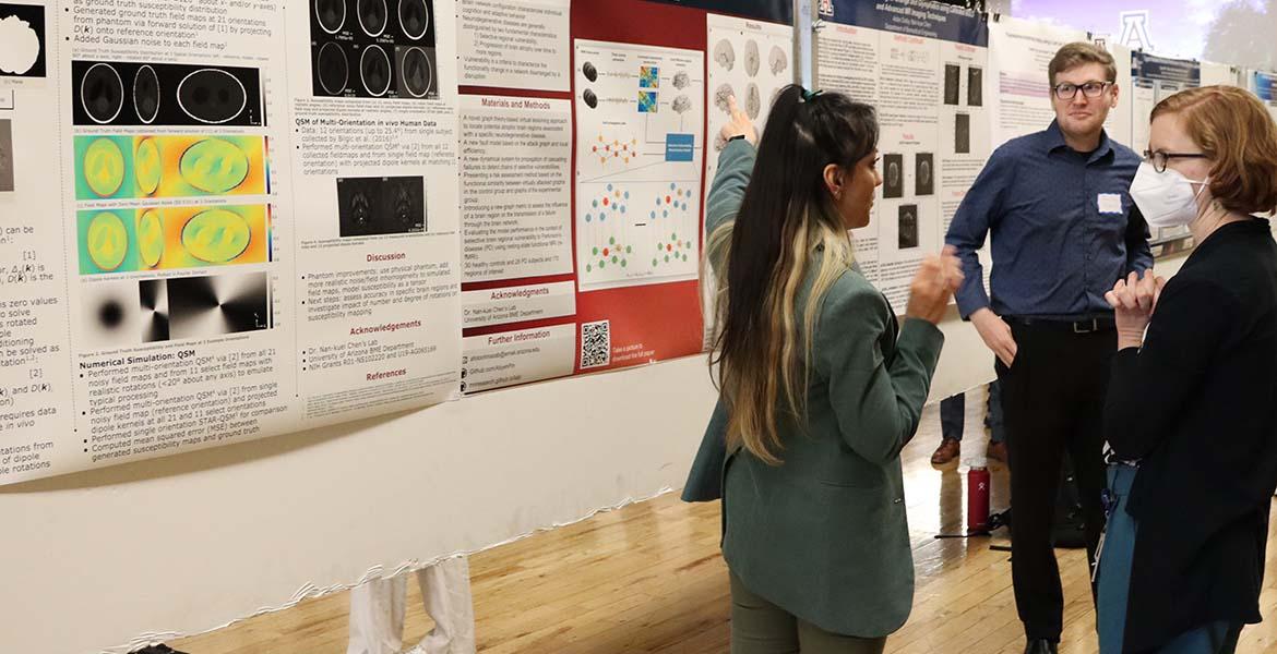 A student gestures at a research poster while two other people look on
