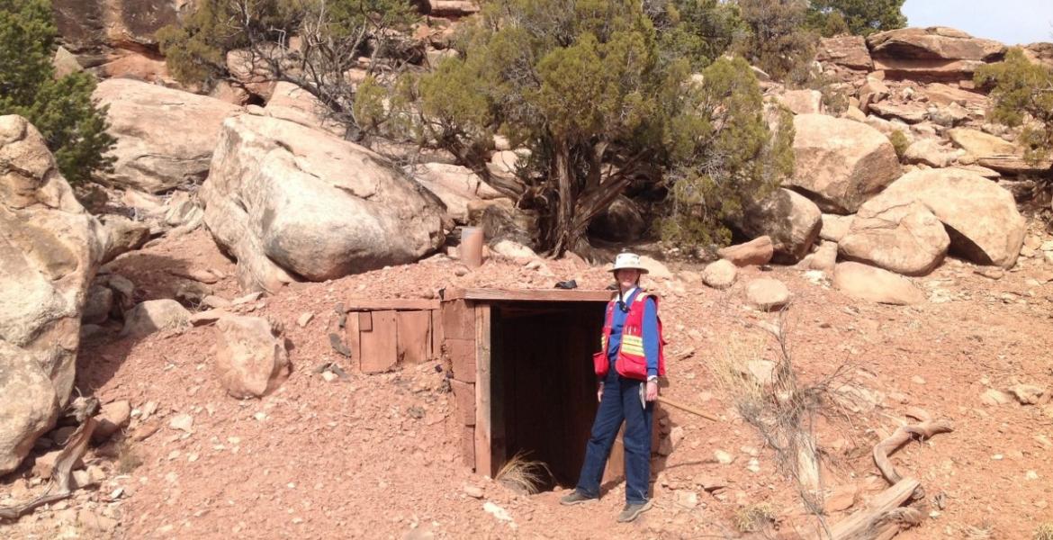 Isabel Barton wearing a red vest and standing next to the entrance of a mine in a desert setting.