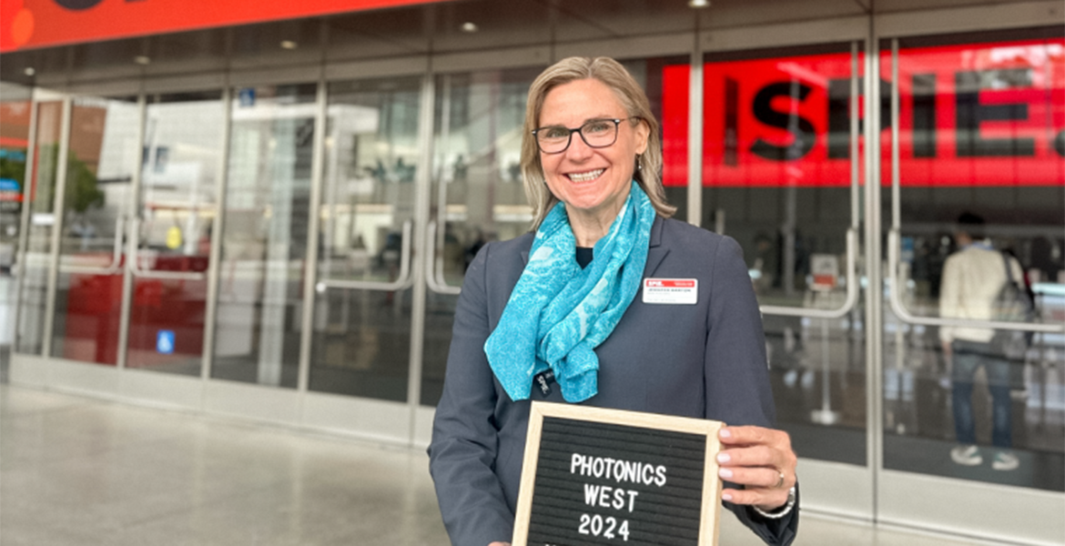 A woman in a blue scarf, Jennifer Barton, holds a sign that reads Photonics West 2024.