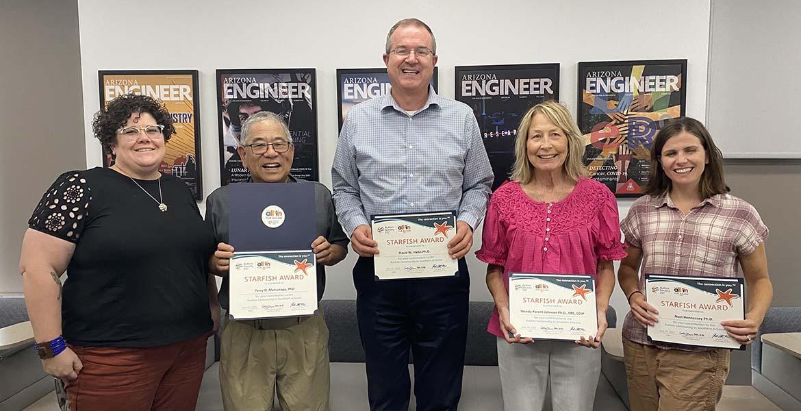 Five people stand indoors with certificates