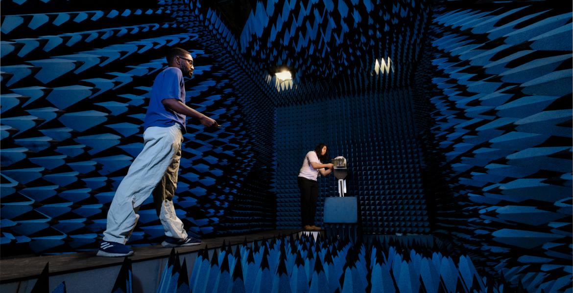 Two young men stand in a room covered in spikes of blue foam on all four walls, the floor and ceiling.