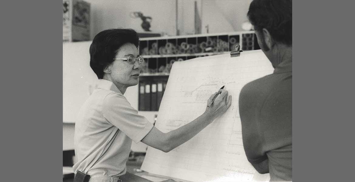 Frances Walker explaining a blueprint on a large white sheet of paper to an onlooker.