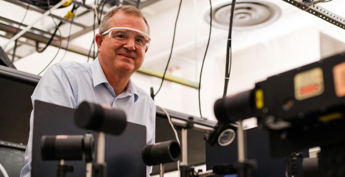 David Hahn smiling and wearing safety glasses, leaned over optics equipment