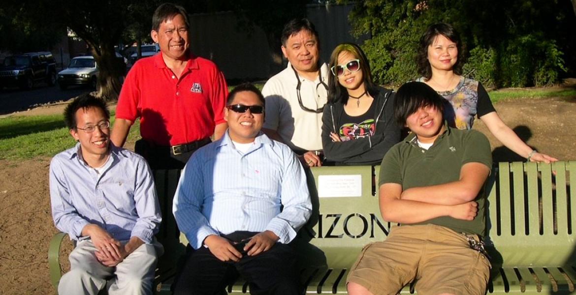 A family group of 7 gathers around a memorial bench on the University of Arizona campus