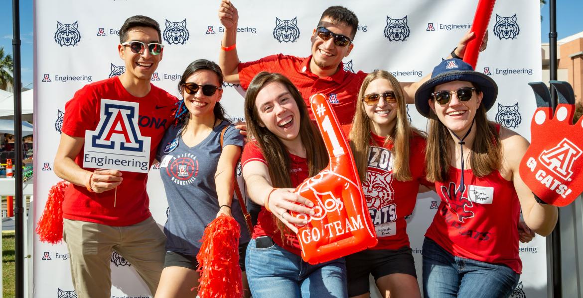 A group of people in Arizona Wildcats gear holding up an inflated #1 finger, pom poms and a UArizona Engineering logo