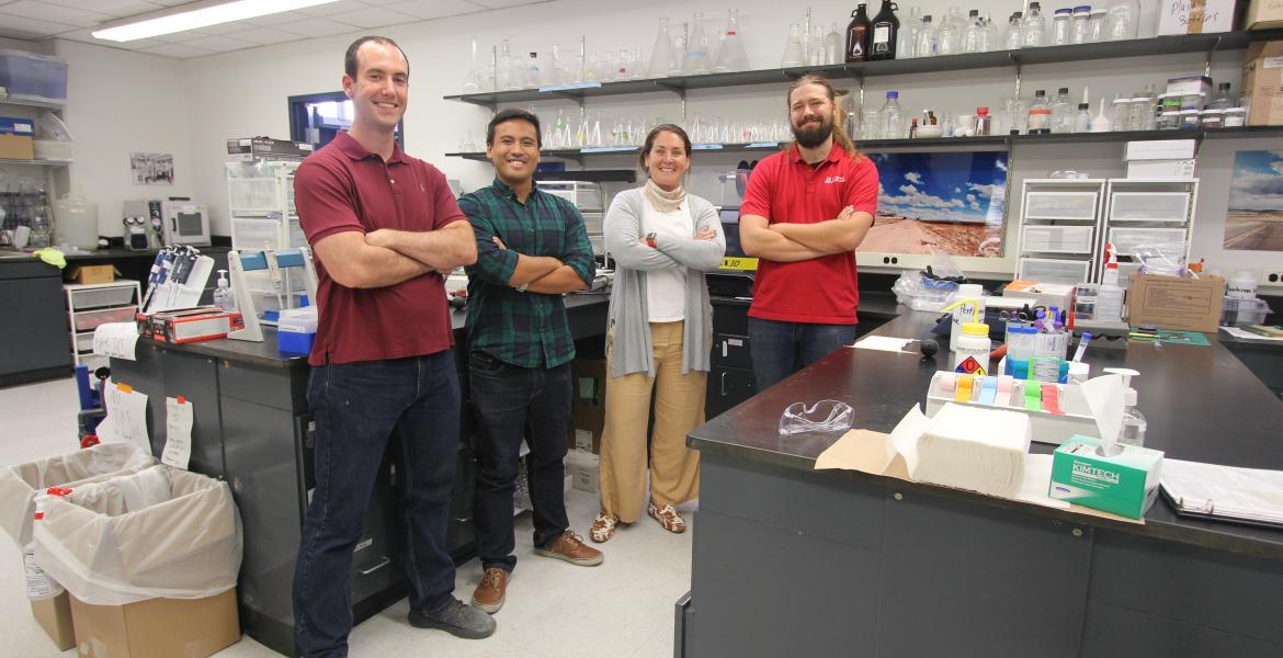 Four people stand with their arms crossed, smiling, in a chemistry laboratory.