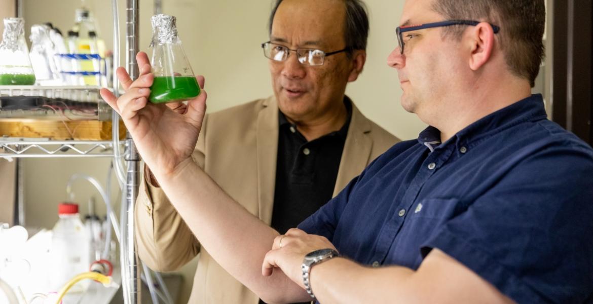 Two men examine a beaker of algae.