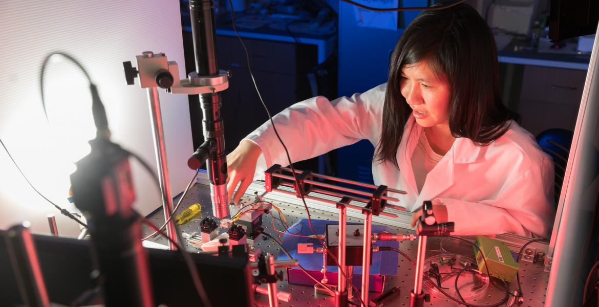 Judith Su wearing a white labcoat and leaned over a complicated array of sensors.