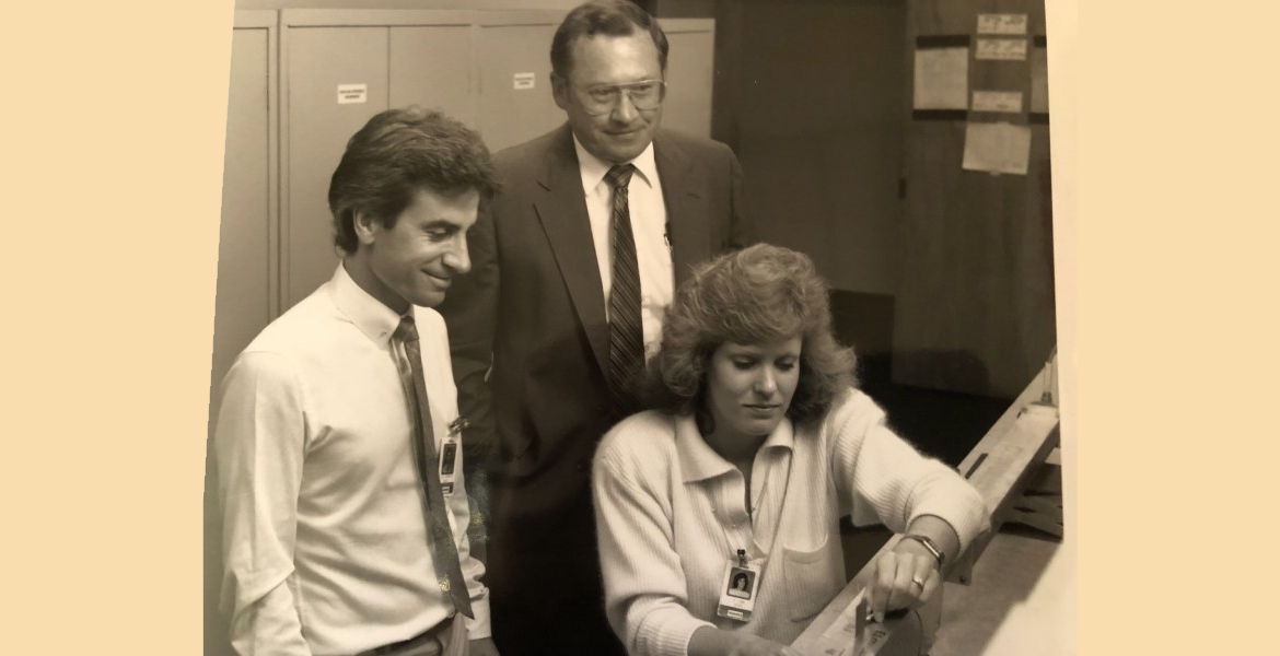 Black and white photo of two men and a woman leaned over a computer