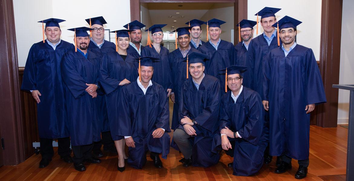 A group of 15 men and women wearing blue graduation caps and gowns