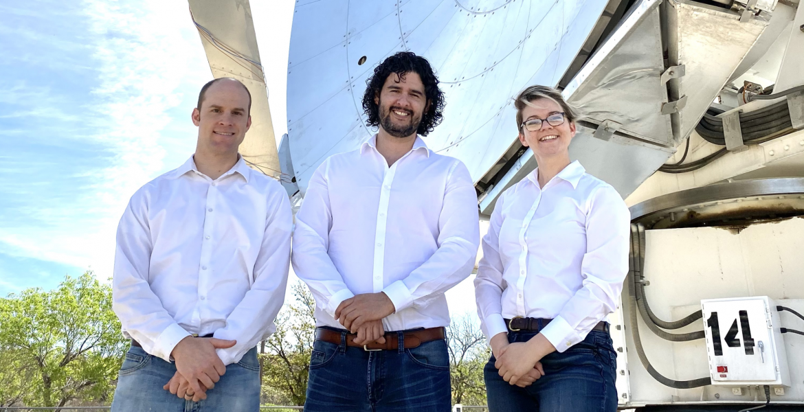 Three people in white shirts stand in front of a large, shiny telescope.