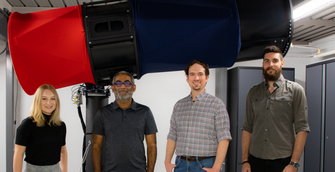 Four people stand in front of a large red and blue telescope.