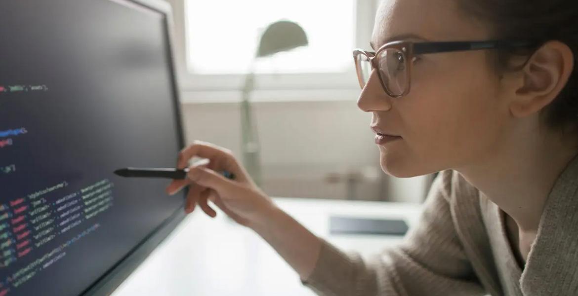 A woman leans over a computer screen, examining lines of code.