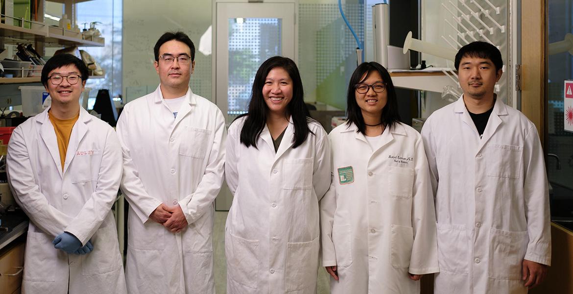 Five people in white lab coats pose for a photo in a lab.