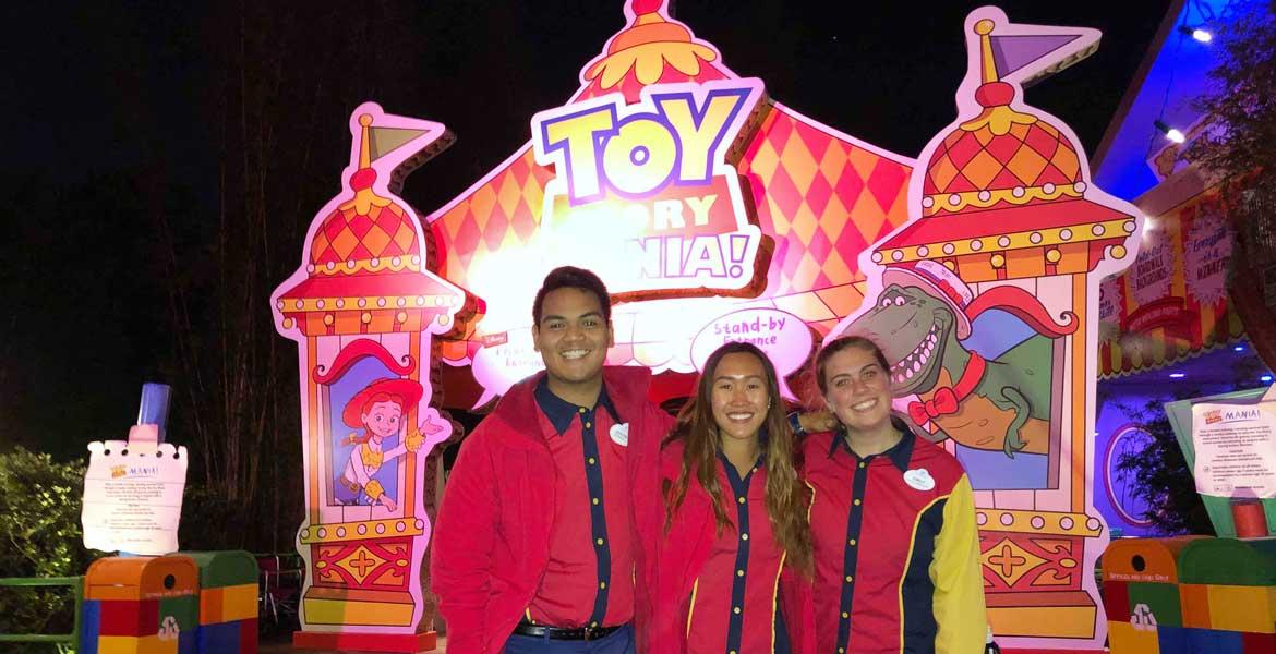 Three smiling people in Disney uniforms in front of the Toy Story Mania! attraction.