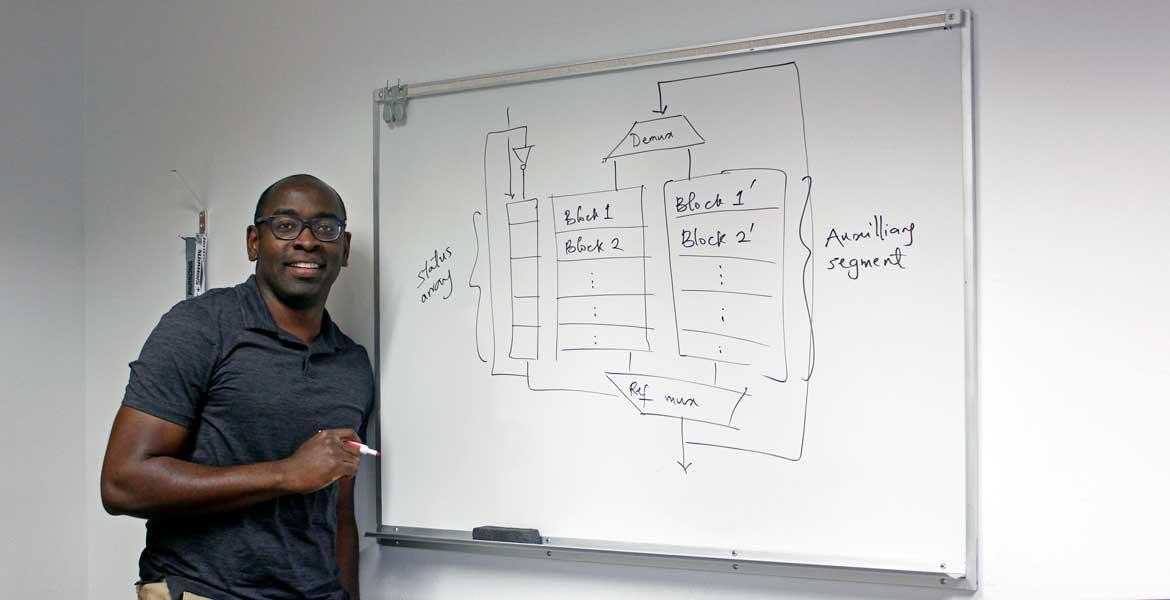 Tosiron Adegbija stands at a whiteboard with a diagram of computer memory caching written on it in black marker