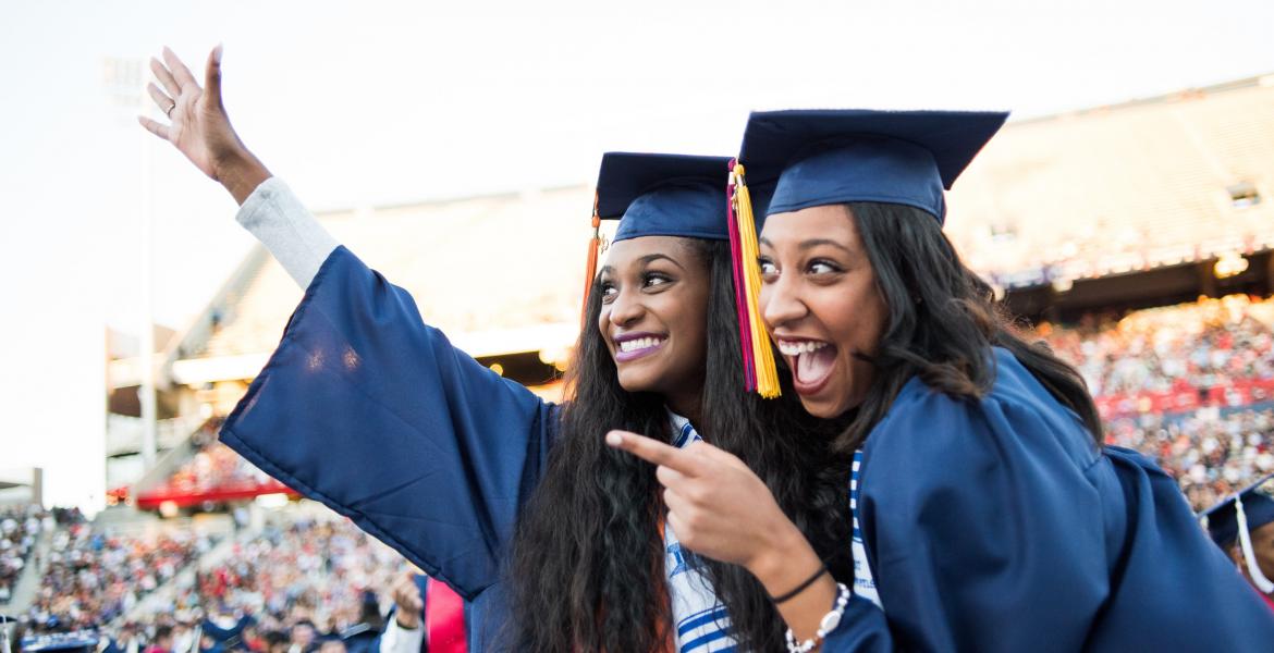 Two women wearing caps and gowns pose for a photo at graduation.