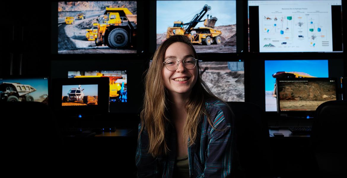 a student poses in front of several screens running mining software