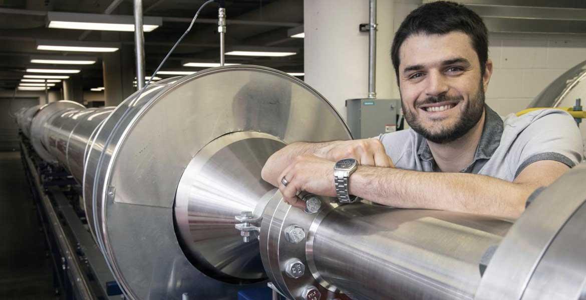Alex Craig smiles and rests his arm on a 104-foot silver wind tunnel