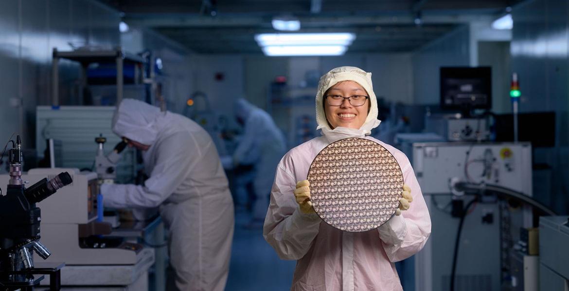 A student in a gown holds a test wafer in the clean room