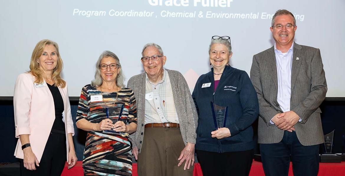 Five people pose with two award statues