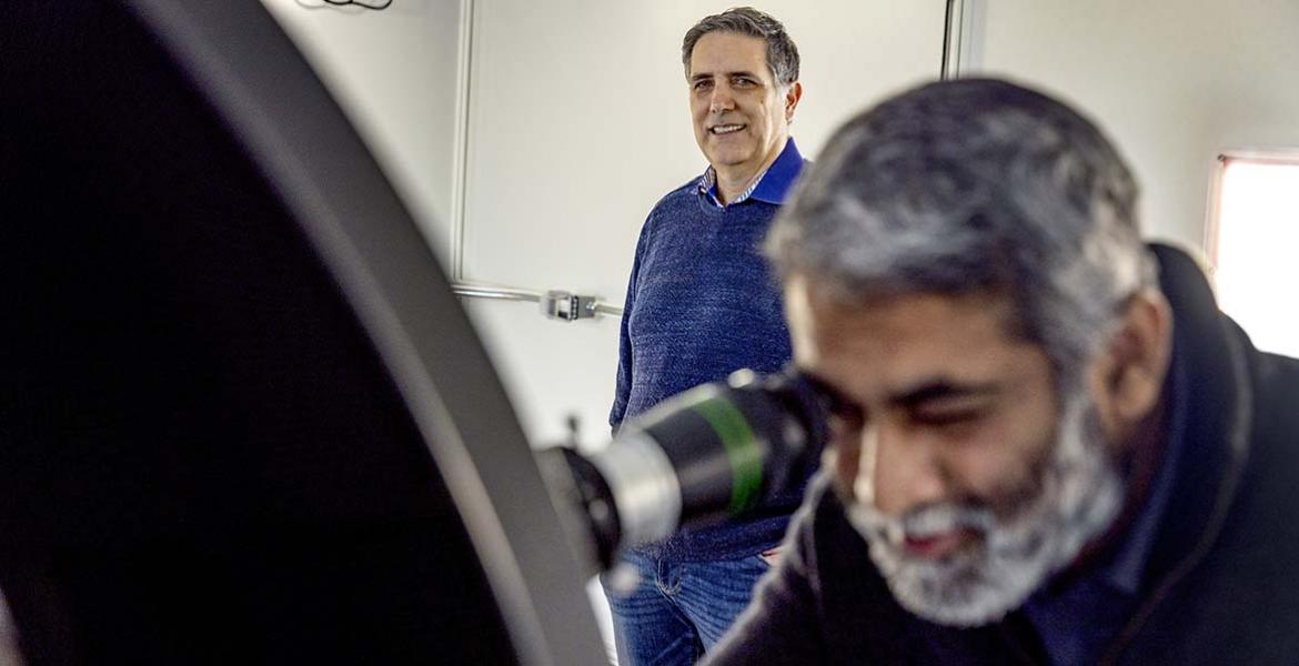 a scientist uses an optical instrument while another stands by