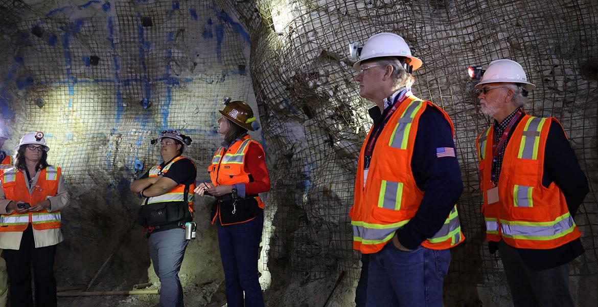 5 people wearing hard hats stand inside a mind